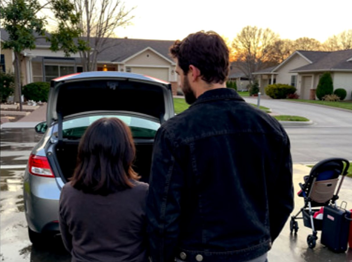 Couple at an open car trunk on a wet driveway at sunset